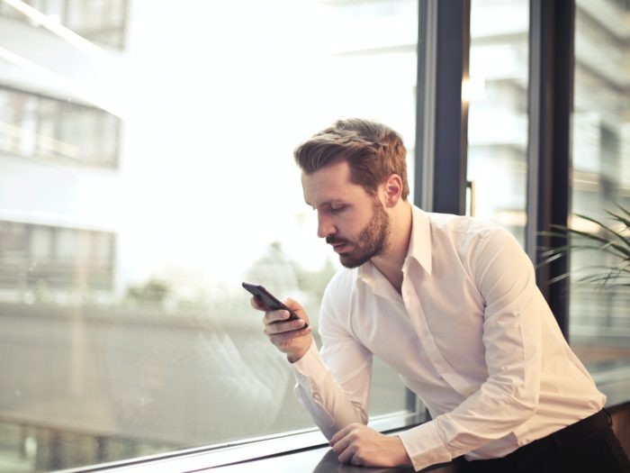 photo-of-man-in-white-dress-shirt-holding-phone-near-window-859265